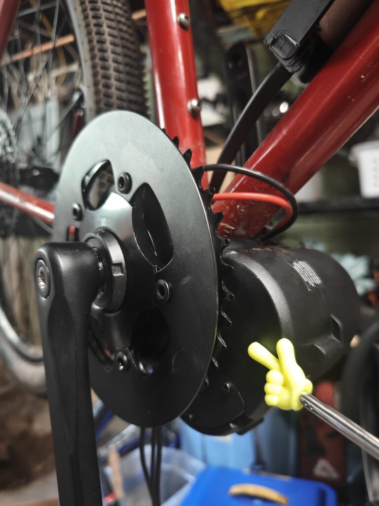 Photo of a new electric mid drive motor mounted to an old steel red mountain bike.
